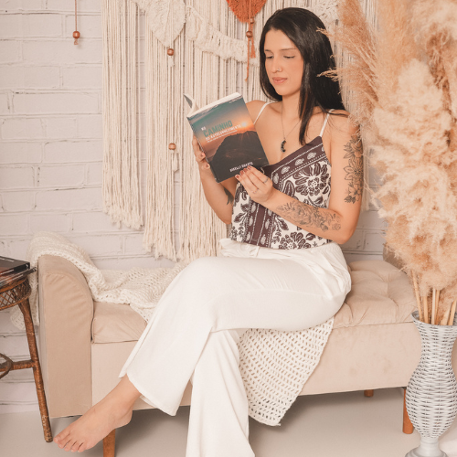 Giselli Duarte lendo um livro em ambiente com cortinas de macramê.